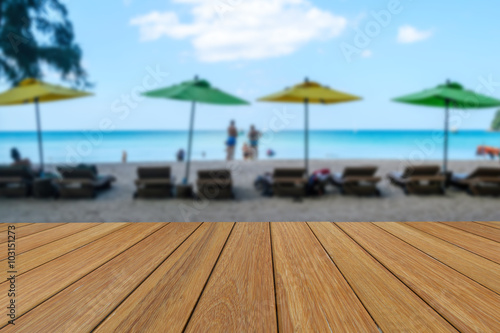 Wood table top on blurred colorful of umbrella and white sand beach background with some people