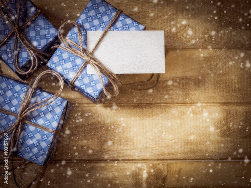 Top view of gift box in blue paper decorated with linen cord and sticker with place for customer's note on the wooden table. Drawn snow. Dark toned