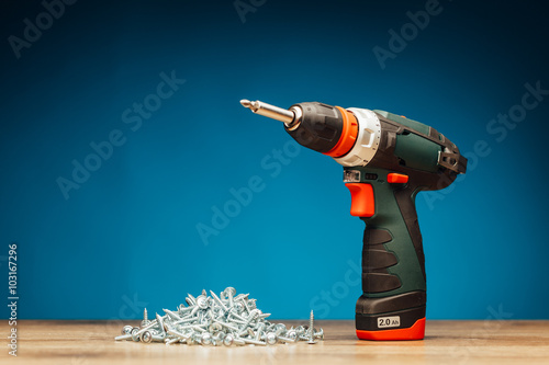 cordless screwdriver and fasteners screws on blue background photo