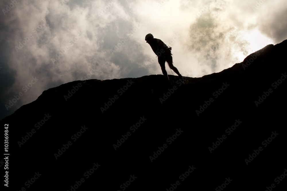 Man walking on the top of a hill after climbing with clouds in backrgound.