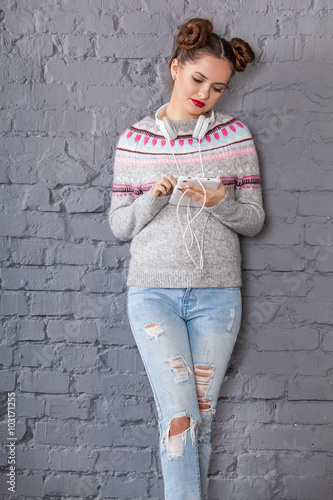 Portrait of a stunning young woman posing by the grey brick wall. Jeans style. Beauty, fashion