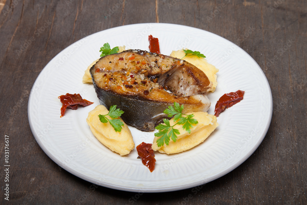 Fried tuna fish with mashed potato, dried tomato and parsley on