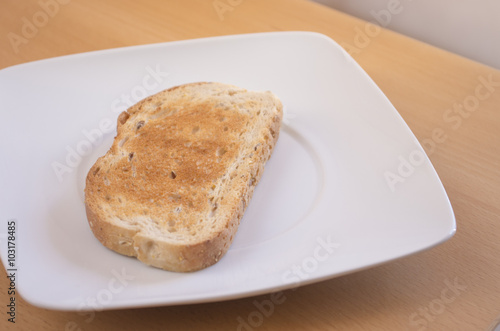 Tostada de pan en un plato blanco con luz natural encima de una mesa. Desayuno.