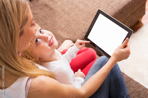 Little girl looking up to mother while they are using tablet 