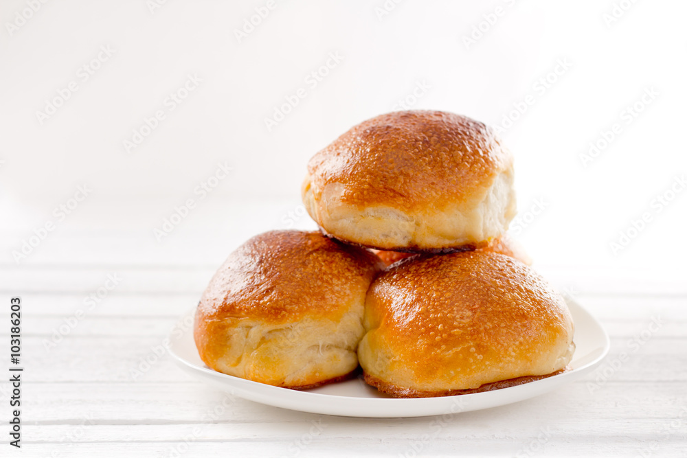 Three rosy appetizing buns on a plate on a white background natural Three rosy appetizing buns on a plate on a white background natural
