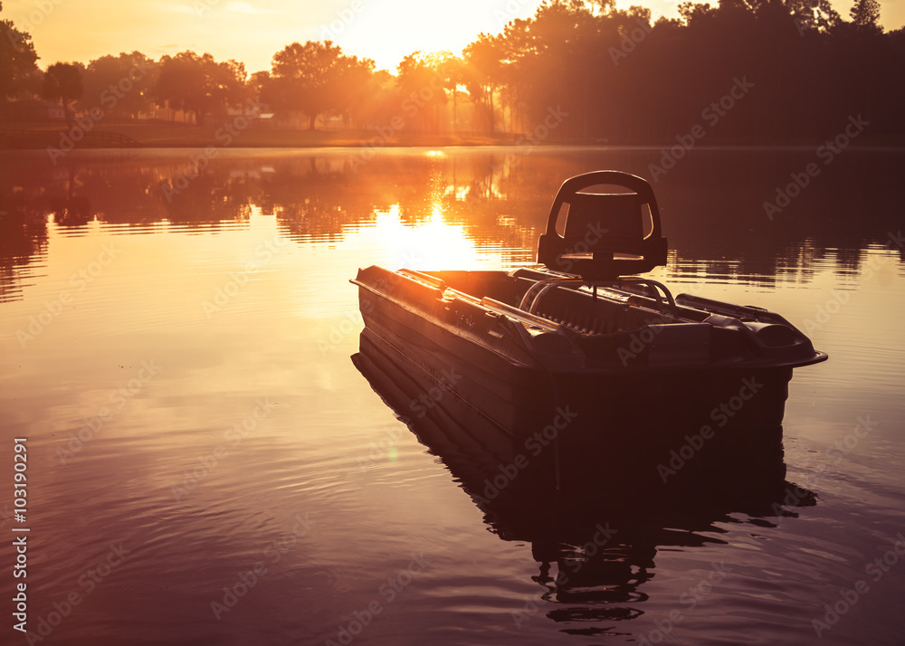 Small empty fishing boat on lake river water pond at sunrise sunset dawn  early morning dusk with sun rays and trees forest on horizon feeling  peaceful relaxed serene calm meditative Stock Photo
