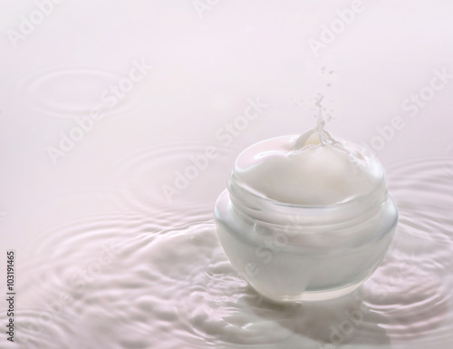 Moisturizing cosmetic  cream  stands on the pink milk background with milk splash