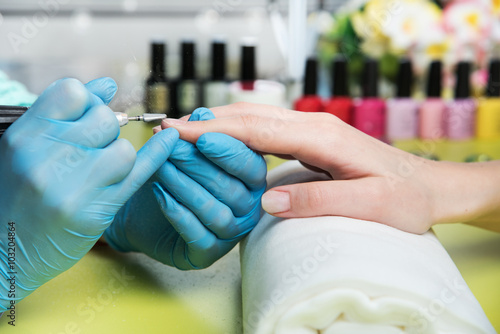 Closeup shot of a woman in a nail salon receiving a manicure by a beautician with nail file. Woman getting nail manicure. Beautician file nails to a customer photo