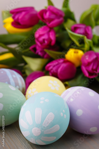 Easter painted eggs on wooden light background with spring bouquet tulips