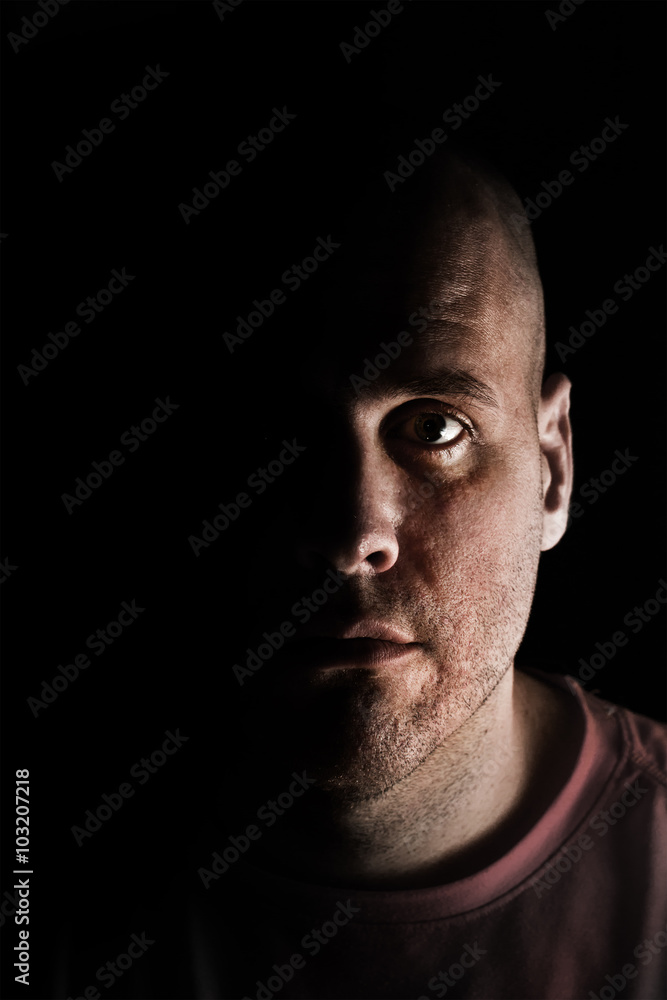 Fototapeta premium Adult Caucasian white man in deep shadows scruffy and unshaven looking at camera mysteriously while tired exhausted