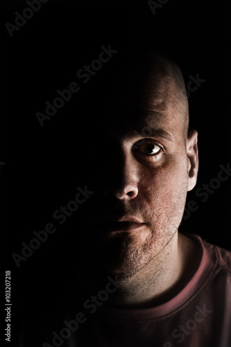 Adult Caucasian white man in deep shadows scruffy and unshaven looking at camera mysteriously while tired exhausted