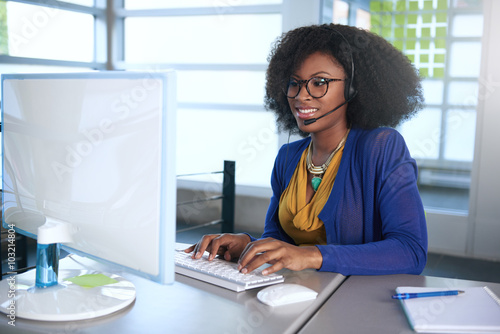 Portrait of a smiling customer service representative with an afro at the computer using headset