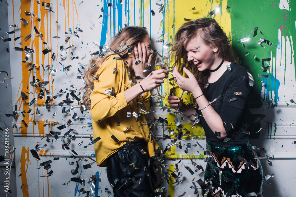 two friends at the wall with champagne in a nightclub in confetti