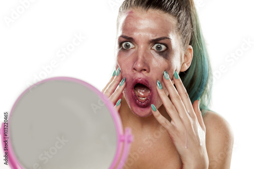 shocked young woman with smeared makeup looks at herself in the mirror