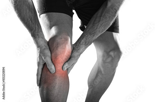 young sport man with athletic legs holding knee with hands in pain after suffering injury running photo