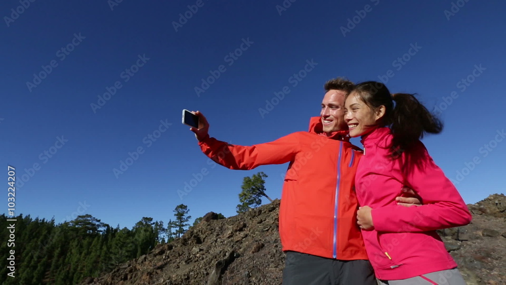Smartphone couple taking selfie photo on hike. Hiking people using smart phone for self portrait picture in mountain nature landscape. Happy multiracial couple having living active healthy lifestyle. Smartphone couple taking selfie photo on hike. Hiking people using smart phone for self portrait picture in mountain nature landscape. Happy multiracial couple having living active healthy lifestyle.