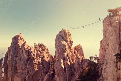 People crossing the chasm on the rope bridge. Black sea background, Crimea, Russia. Image with vintage filter