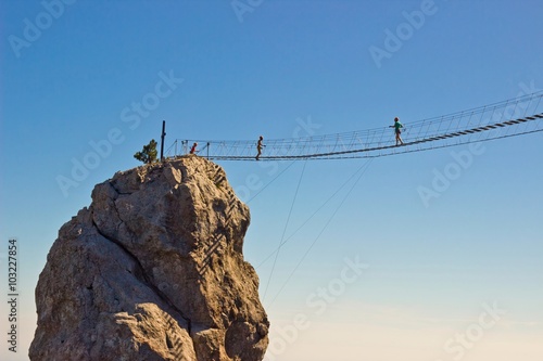 People crossing the chasm on the hanging bridge. Black sea background, Crimea, Russia