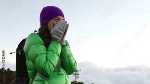 Freezing woman feeling cold outdoors trying to keep warm shaking and shivering wearing hat and gloves outside hiking on hike.