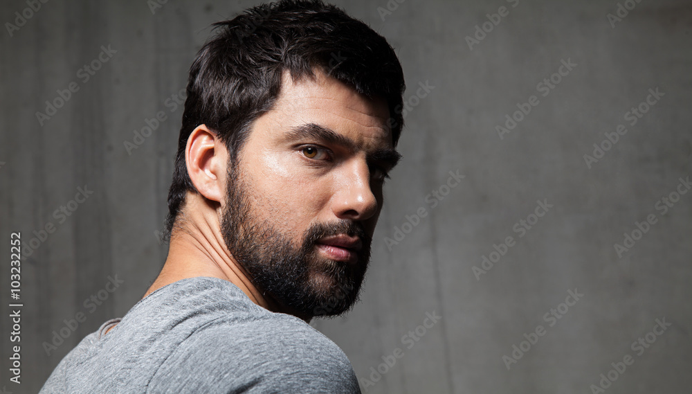 Obraz premium Portrait of handsome bearded guy from behind on a background of a cement wall
