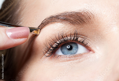 Closeup of a woman pulls out her eyebrows with tweezers photo