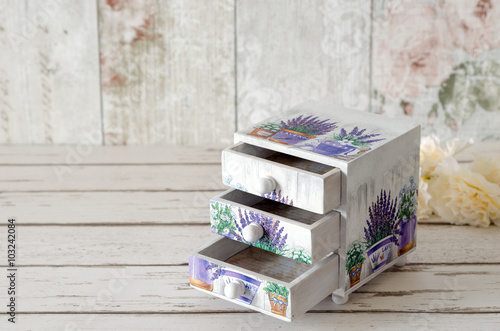 A handmade chest of trinket drawers decoupaged with vintage paperwith pots of Lavender on a rustic wooden background