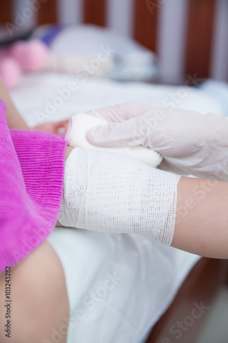 Child injured. Pediatrician doctor bandaging child's knee.