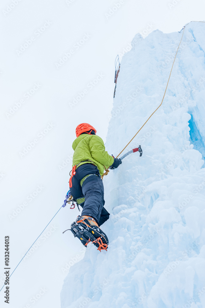 Alpinist man with ice tools axe in orange helmet climbing a lar Alpinist man with ice tools axe in orange helmet climbing a lar