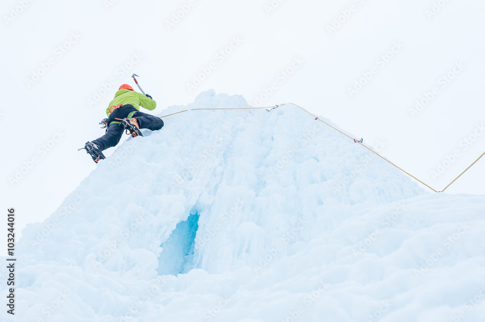 Alpinist man with  ice tools axe in orange helmet climbing a lar