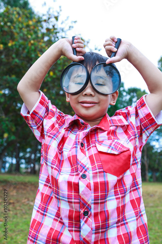 Young boy exploring nature with magnifying glass. Outdoors.