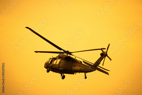 Fotografie Silhouette of the military helicopter  moving into sky at sunset