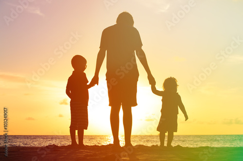 father and two kids walking on beach at sunset