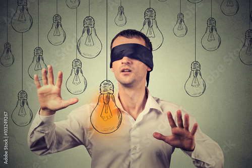 Blindfolded young man walking through light bulbs searching for bright idea photo