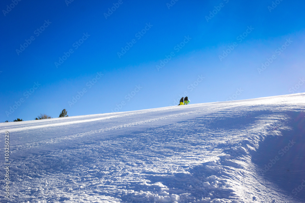 Two snowboarders are climbing the snowy hill toward the sun