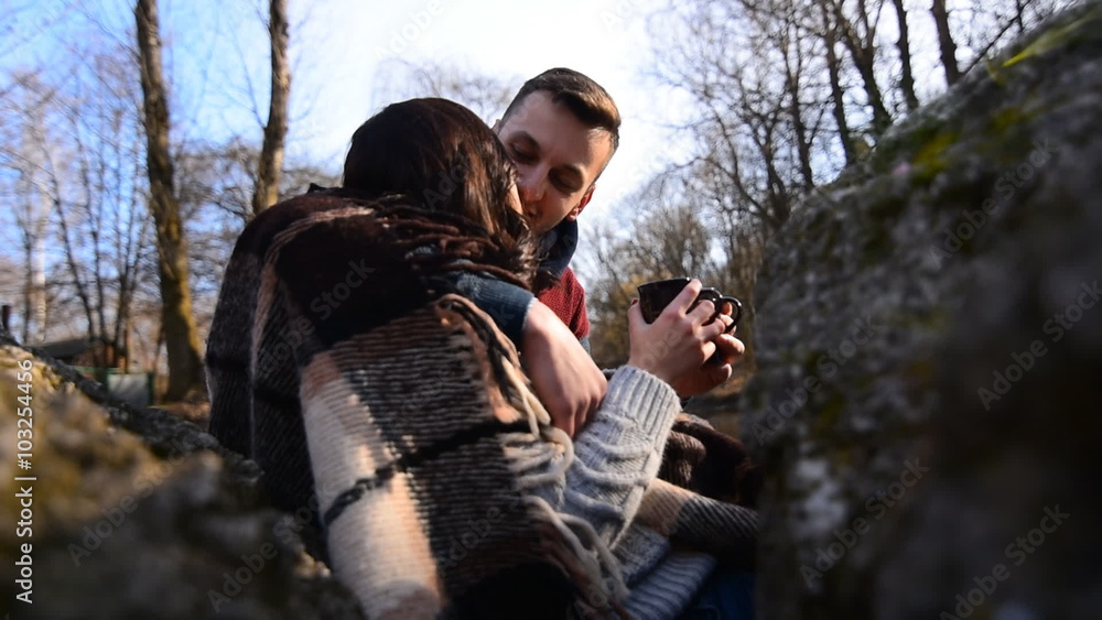 Young happy couple outdoor sitting with cups of hot tea on the stones and kissing, slow motion Young happy couple outdoor sitting with cups of hot tea on the stones and kissing, slow motion