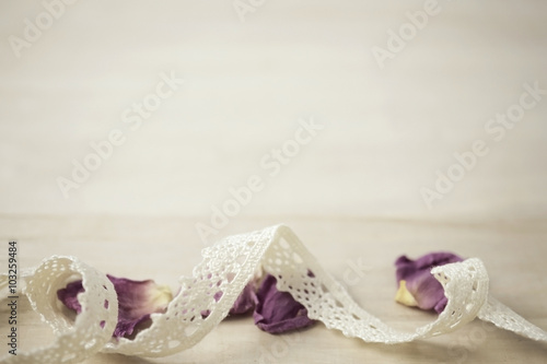 lace and dried rose petals on wooden background in vintage style 