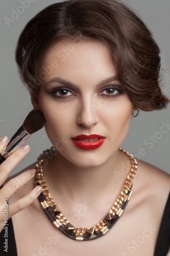 Beautiful woman with evening make up surrounded by the different brushes for make up