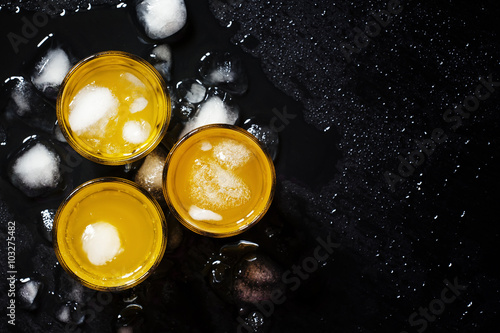 Yellow cocktail with ice on wet dark background, top view