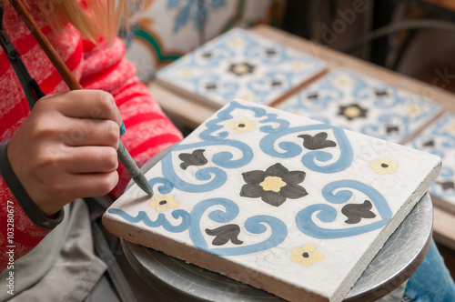 Stampa su tela A pottery decorator painting a ceramic tile with floral motifs in his work table