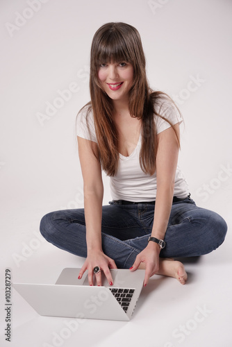 Eine junge Frau, Mädchen sitzt barfuß auf dem Boden und hat einen Laptop vor sich.