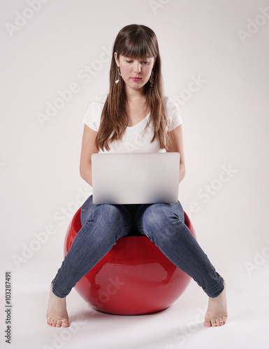 Eine junge Frau, Mädchen sitzt barfuß auf einem rotem Kunststoffsessel und hat einen Laptop in der Hand