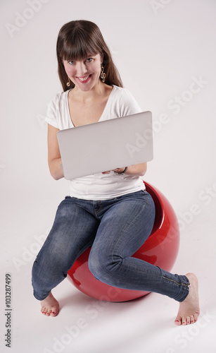 Eine junge Frau, Mädchen sitzt barfuß auf einem rotem Kunststoffsessel und hat einen Laptop in der Hand