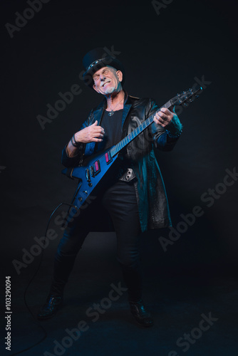 Senior heavy metal man with electric guitar against dark backgro