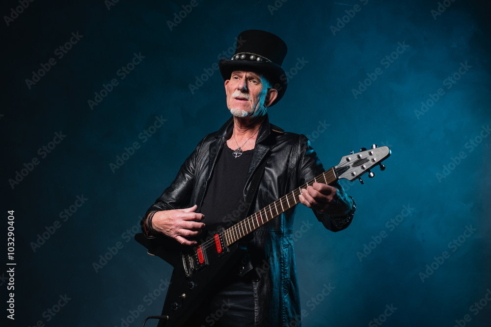Fototapeta premium Heavy metal senior man with electric guitar in front of dark blu