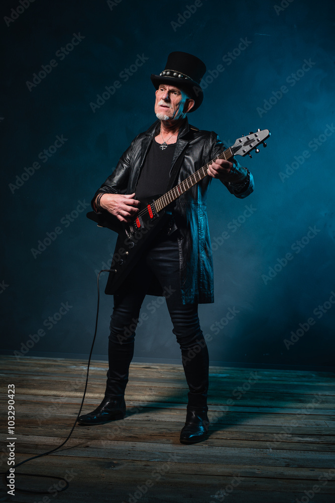 Fototapeta premium Heavy metal senior man with electric guitar in front of dark blu