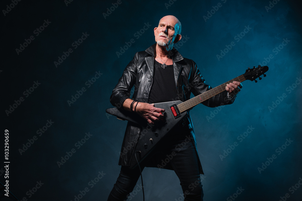 Fototapeta premium Bald heavy metal senior man with electric guitar in front of dar