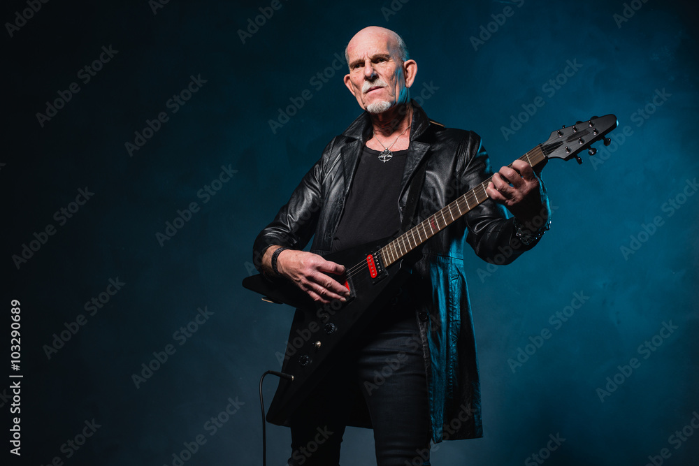 Bald heavy metal senior man with electric guitar in front of dar