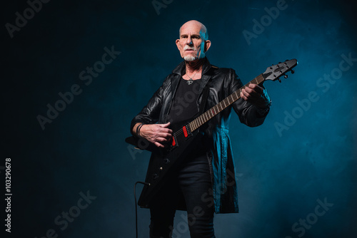 Bald heavy metal senior man with electric guitar in front of dar