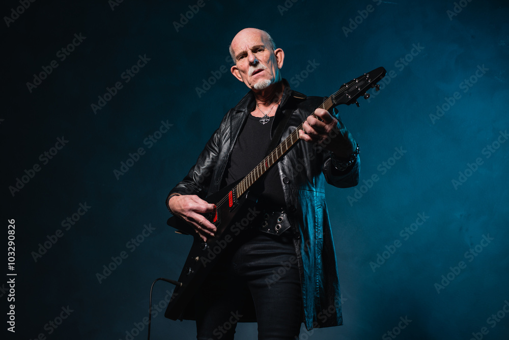 Bald heavy metal senior man with electric guitar in front of dar