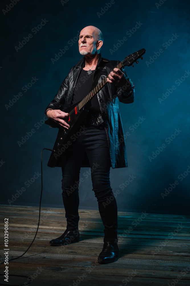 Fototapeta premium Bald heavy metal senior man with electric guitar in front of dar